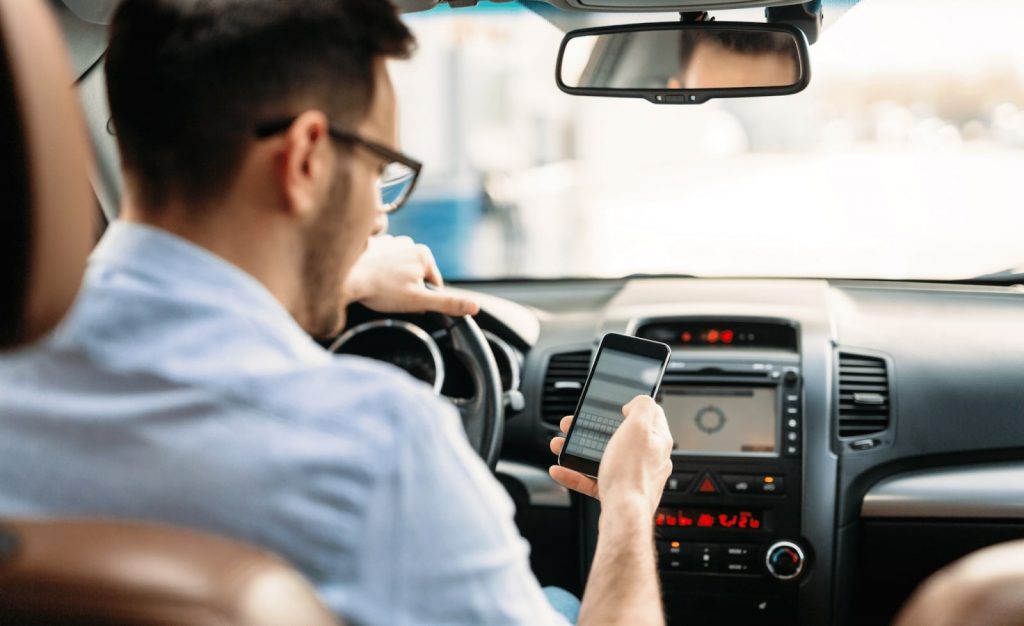 man looking into smartphone while driving